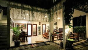 A well-lit indoor space with hanging plants, a reception desk, and a seating area with chairs and a table. - Dewi Villa Padangbai Hotel (Padangbai)