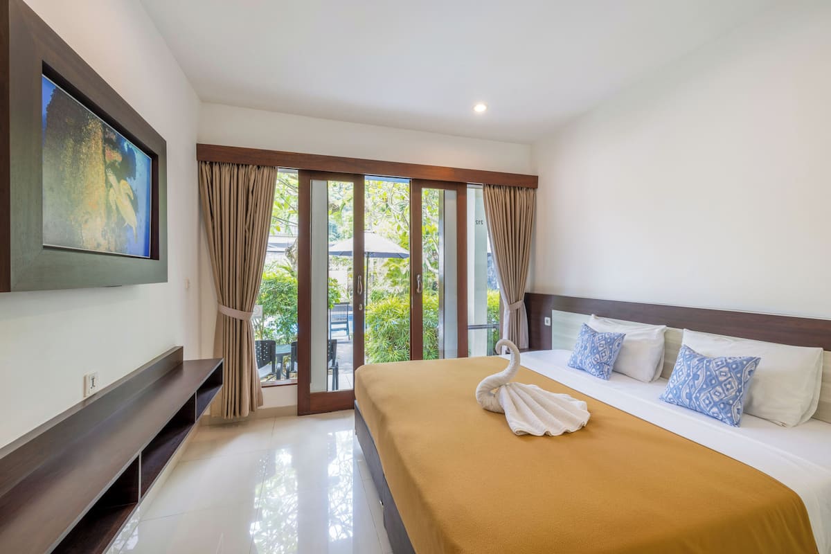 A hotel room with a large bed, a TV mounted on the wall, and a sliding glass door leading to an outdoor area.