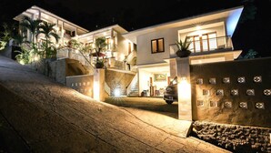 A modern two-story house with a well-lit entrance, a staircase, and a balcony. - Dewi Villa Padangbai Hotel (Padangbai)