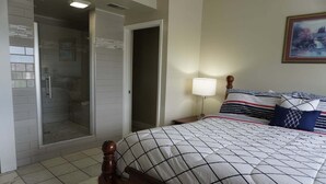 Quarto com cama, mesa de cabeceira, luminária, chuveiro e porta.
