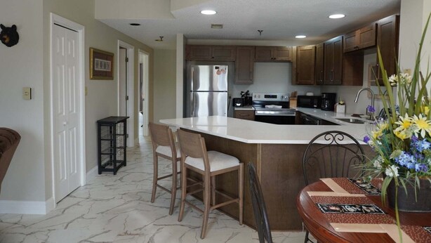 A kitchen with a large island, bar stools, and a dining table with a floral centerpiece. - City View 411 3BD Condo with Fireplace by RedAwning (Pigeon Forge)
