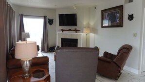 Uma sala de estar com lareira, uma televisão montada acima e um enfeite de cabeça de urso na parede.