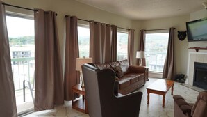 Uma sala de estar com um sofá de couro, uma mesa de centro de madeira e uma televisão fixada na parede.