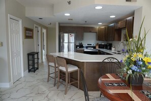 A kitchen with a central island, wooden chairs, a dining table with a floral centerpiece, and a refrigerator.
