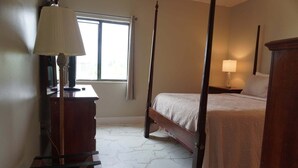 A four-poster bed with a wooden frame, a bedside table with a lamp, a dresser, and a window with curtains. - City View 411 3BD Condo with Fireplace by RedAwning (Pigeon Forge)