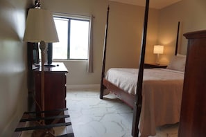 A four-poster bed with a wooden frame, a bedside table with a lamp, a dresser, and a window with curtains. - City View 411 3BD Condo with Fireplace by RedAwning (Pigeon Forge)