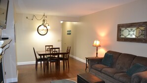 Ein Wohnzimmer mit einem braunen Sofa, einem Esstisch mit Stühlen, einer Uhr und einer Lampe.