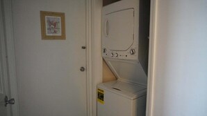 A laundry room with a door, a framed picture on the wall, and a warning label on the washing machine. - Smoky Mountains 711 3BD Condo with All Round Private Balcony by RedAwning (Pigeon Forge)
