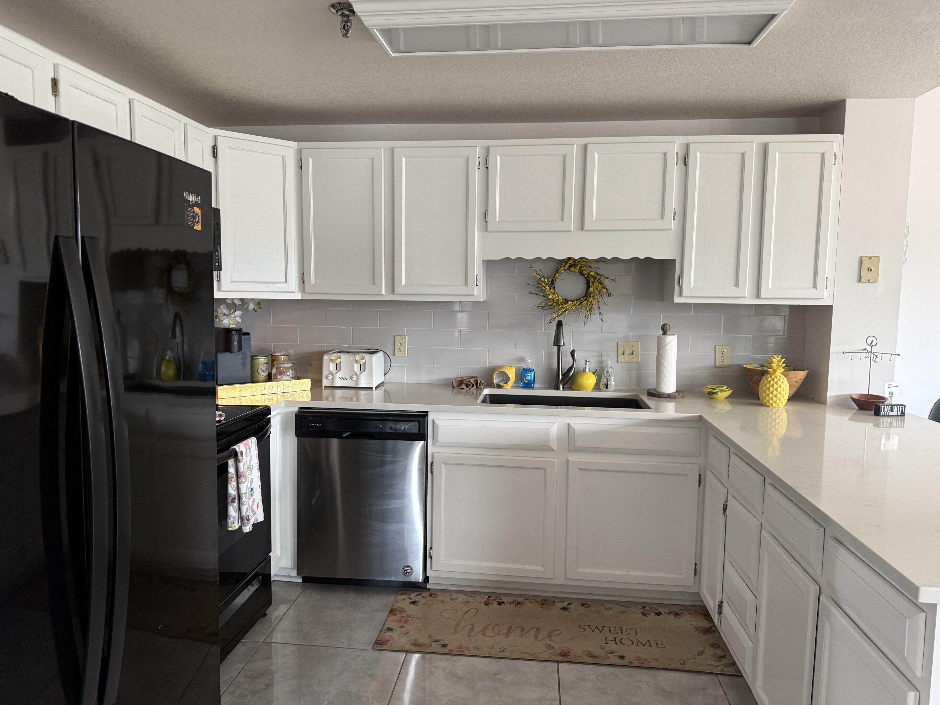 Una cocina con armarios blancos, un refrigerador negro, un lavavajillas de acero inoxidable y un lavabo con grifo.