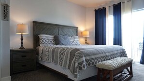 A bedroom with a bed, bedside lamps, a bench, a nightstand, and a 'HOME' sign on the wall. - Smoky Mountains 711 3BD Condo with All Round Private Balcony by RedAwning (Pigeon Forge)