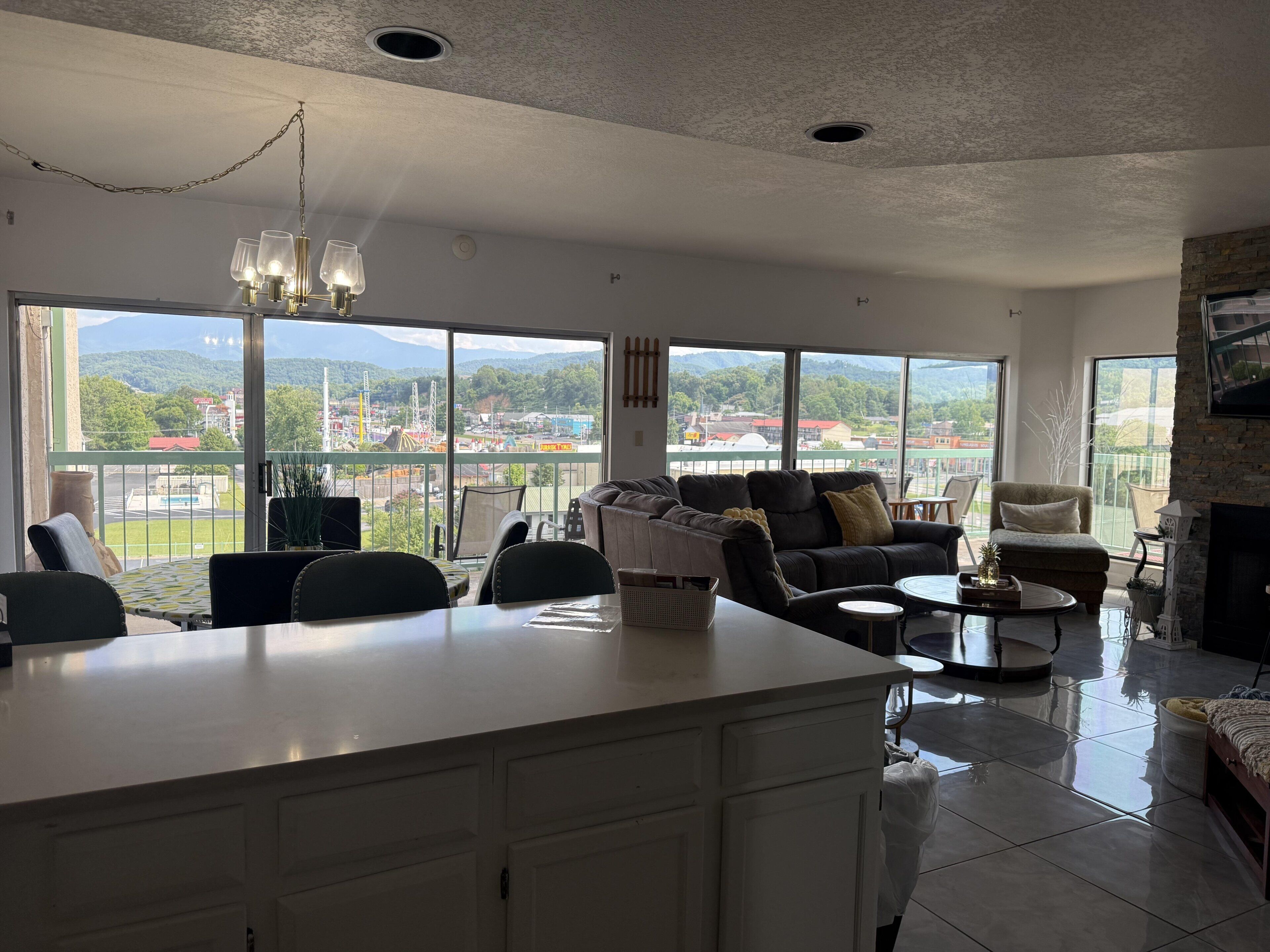 A spacious living area with a large island, seating, and a view of a park and buildings.