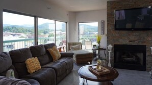 A modern living room with a leather sofa, a round coffee table, a fireplace, and a TV mounted on a brick wall. - Smoky Mountains 711 3BD Condo with All Round Private Balcony by RedAwning (Pigeon Forge)