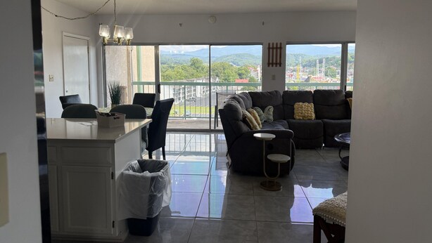 A spacious living area with a sofa, a small table, and a view of a parking lot and mountains. - Smoky Mountains 711 3BD Condo with All Round Private Balcony by RedAwning (Pigeon Forge)