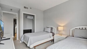 A bedroom with two beds, a wardrobe, a desk with a lamp, and a TV.