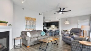 A modern living room with a fireplace, grey sofas, a coffee table, and a kitchen in the background.