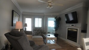 Ein Wohnzimmer mit Deckenventilator, Flachbildfernseher, Kamin, Sofa, Couchtisch und Ohrensessel mit Muster.