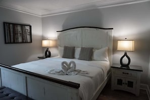 A neatly made bed with a heart-shaped towel arrangement, two bedside lamps, a small cabinet, and a wall-mounted artwork. - Smoky Mountains 304 2BD Condo with Private Balcony and Fireplace by RedAwning (Pigeon Forge)