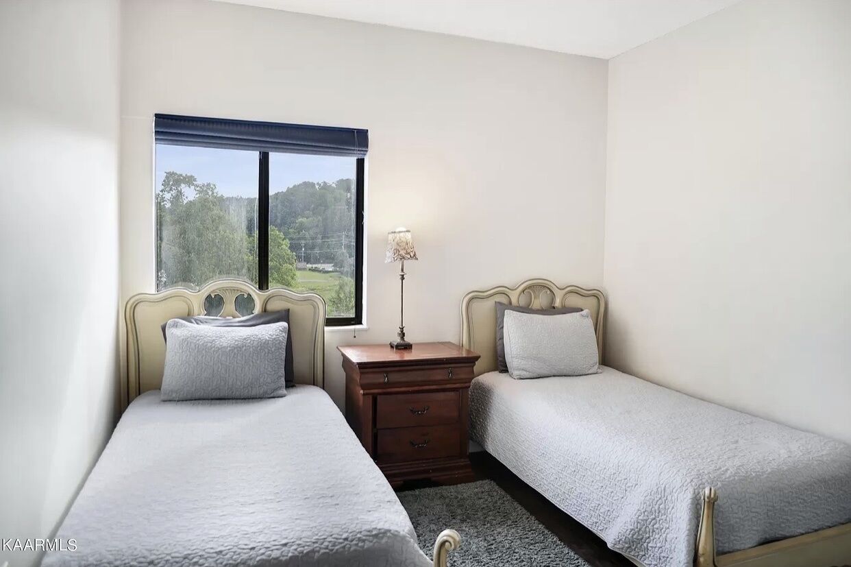 Une chambre avec deux lits simples, une table de chevet avec une lampe et une fenêtre donnant sur des arbres.