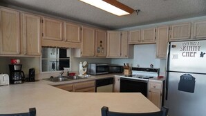A kitchen with wooden cabinets, a refrigerator with a menu magnet, a microwave, a toaster, and a coffee maker. - City View 410 3BD Condo with Private Balcony by RedAwning (Pigeon Forge)