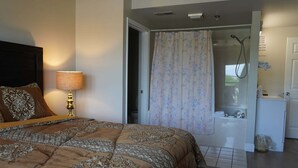 A bedroom with a bed, a nightstand, a lamp, a shower area, and a bathroom. - City View 410 3BD Condo with Private Balcony by RedAwning (Pigeon Forge)