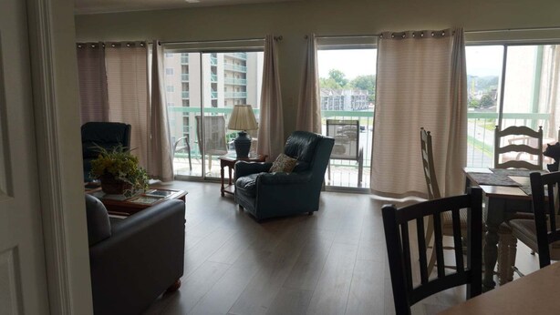 A living room with a sofa, a chair, a table, and a lamp. There is a balcony with a view of buildings and a chair. - City View 410 3BD Condo with Private Balcony by RedAwning (Pigeon Forge)