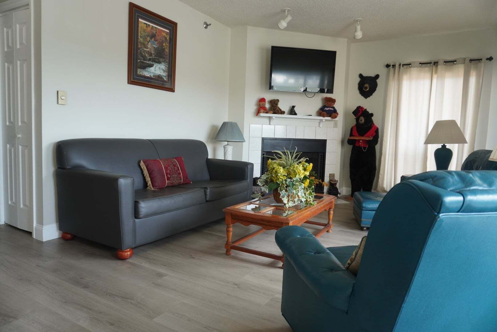 Un salon comprenant un canapé, un fauteuil bleu, une cheminée, un téléviseur et une statue d’ours.