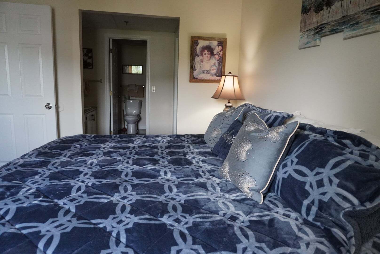 Ein Schlafzimmer mit Bett, einer Tür, einem Badezimmer und einem Bild an der Wand.