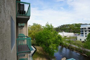 A multi-story building with balconies, a river, and surrounding greenery. - Little Pigeon River 508 2BD Condo with Fireplace and Jacuzzi Tub by RedAwning (Pigeon Forge)