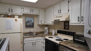 A compact kitchen with white cabinets, a stove, a sink, and a coffee maker. - Little Pigeon River 508 2BD Condo with Fireplace and Jacuzzi Tub by RedAwning (Pigeon Forge)