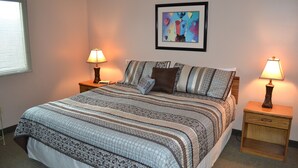 A neatly made bed with a patterned bedspread, two bedside tables with lamps, a framed abstract painting on the wall, and a window with blinds. - Little Pigeon River 602 2BD Condo with Private Balcony by RedAwning (Pigeon Forge)