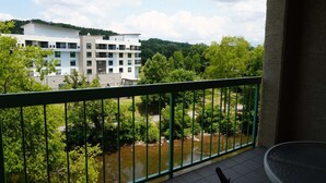 Ein Balkon mit Blick auf einen Fluss, viel Grün und ein modernes Gebäude im Hintergrund.