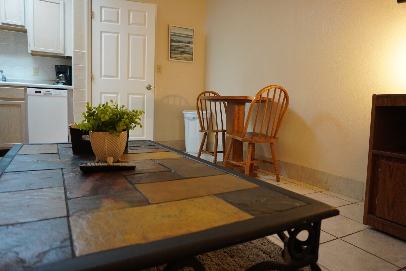 A dining area with a table, chairs, a potted plant, a coffee maker, and a dishwasher.