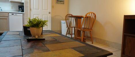 A dining area with a table, chairs, a potted plant, a coffee maker, and a dishwasher.