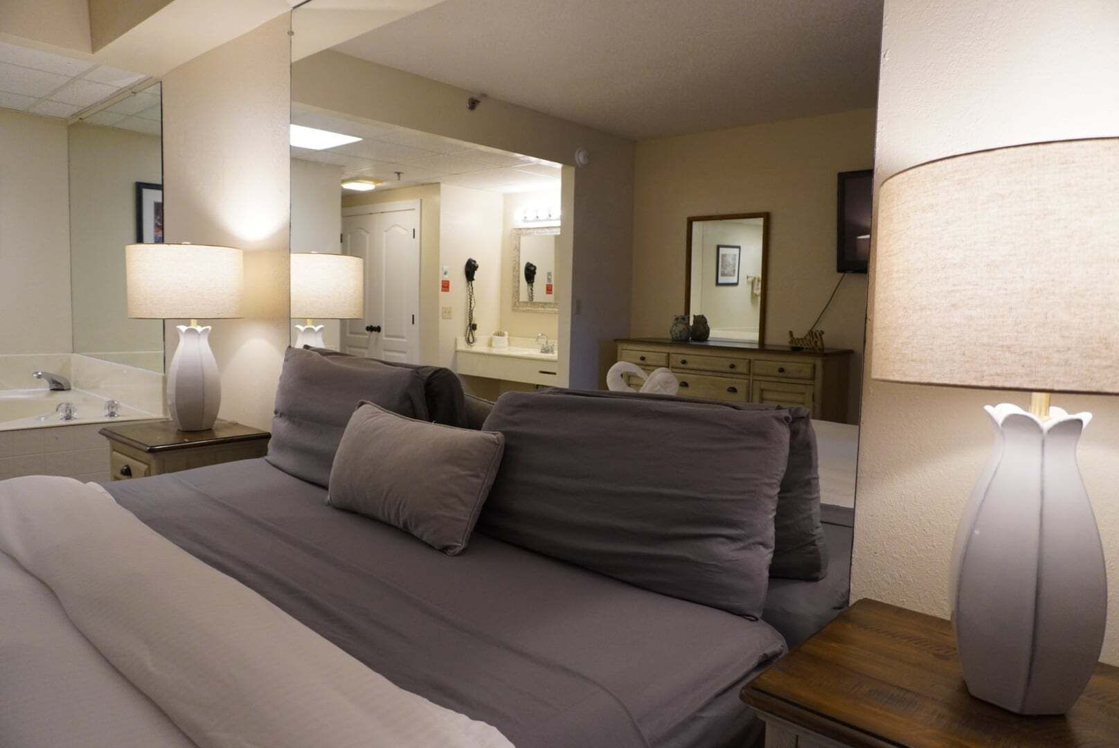 Una camera d'albergo con un letto grande, due comodini, uno specchio, una cassettiera e un bagno con vasca e lavandino.