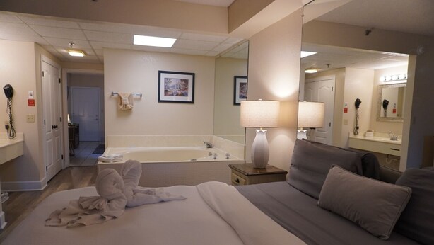 Ein Hotelzimmer mit einem großen Bett, einer Sitzecke mit einer Couch, einem Badezimmer mit einer Badewanne und einem Spiegel.