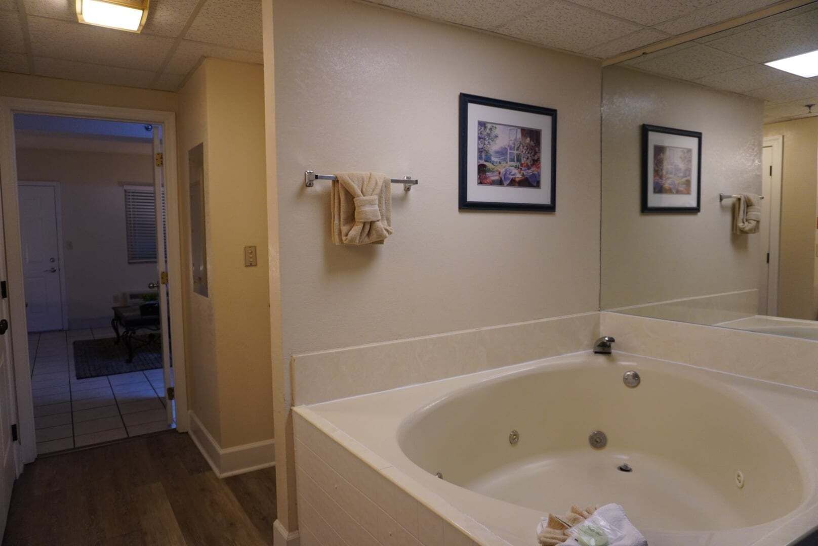 A bathroom with a large bathtub, a towel rack with a towel, and two framed pictures on the wall.