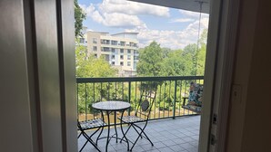 Un balcon avec une table et des chaises, un fauteuil suspendu et une vue sur un immeuble et des arbres.