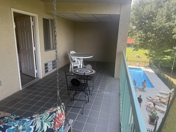 A balcony with a tiled floor, a small round table with chairs, a hanging chair, and a view of a swimming pool. - Little Pigeon River 309 1BD Condo with River View Private Balcony by RedAwning (Pigeon Forge)