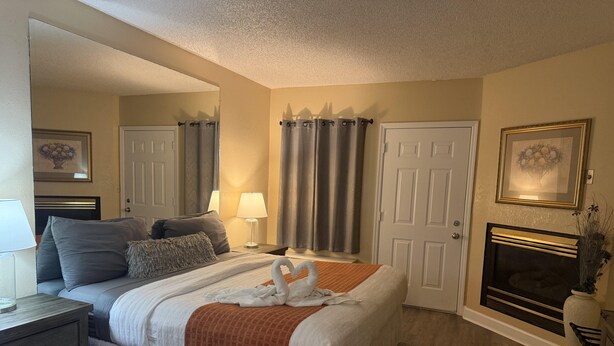Une chambre à coucher bien rangée, avec un lit, des tables de chevet, une lampe, une cheminée et une porte.