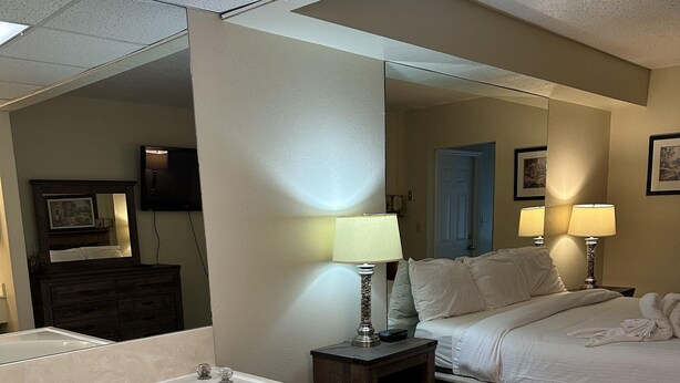 A hotel room with a large bathtub, a bed, a bedside table with lamps, and a mirror. - 609 1bd 1 Bedroom Condo by RedAwning (Pigeon Forge)