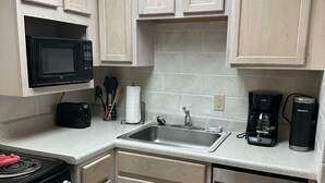 A compact kitchen with light wood cabinets, a black microwave, a coffee maker, and a dishwasher. - 609 1bd 1 Bedroom Condo by RedAwning (Pigeon Forge)