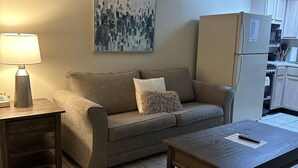 A living room with a sofa, a coffee table, a lamp, and a kitchen area with cabinets and appliances. - 609 1bd 1 Bedroom Condo by RedAwning (Pigeon Forge)