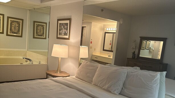 A hotel room with a large bed, two bedside tables with lamps, a full-length mirror, and framed pictures on the wall. - 409 1bd 1 Bedroom Condo by RedAwning (Pigeon Forge)