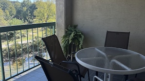 A balcony with a round glass table and four chairs, overlooking a river and greenery. - 409 1bd 1 Bedroom Condo by RedAwning (Pigeon Forge)