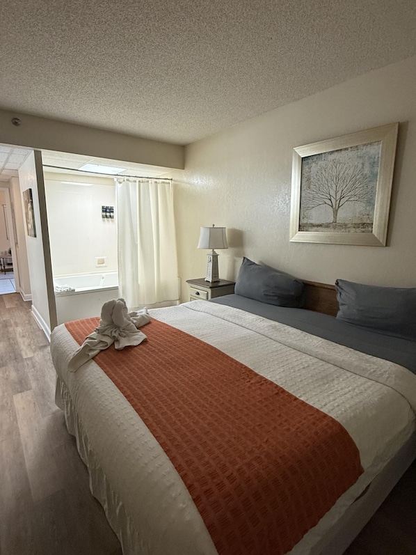 A hotel room with a bed, a nightstand, a lamp, a painting, and a view of the hallway.