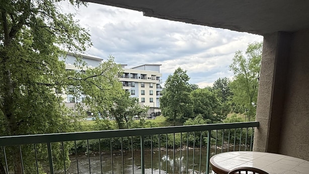 Ein Balkon mit Blick auf einen Fluss, ein Esstisch mit Stühlen und ein Gebäude im Hintergrund.