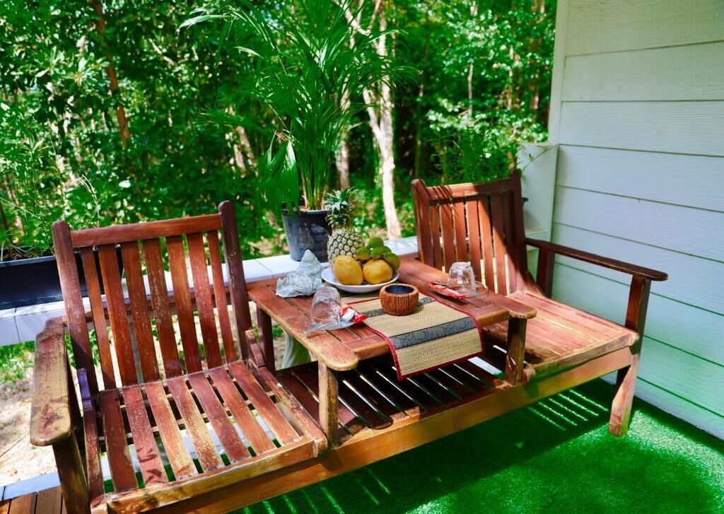 A wooden bench with two chairs, a table, and a potted plant with fruits.
