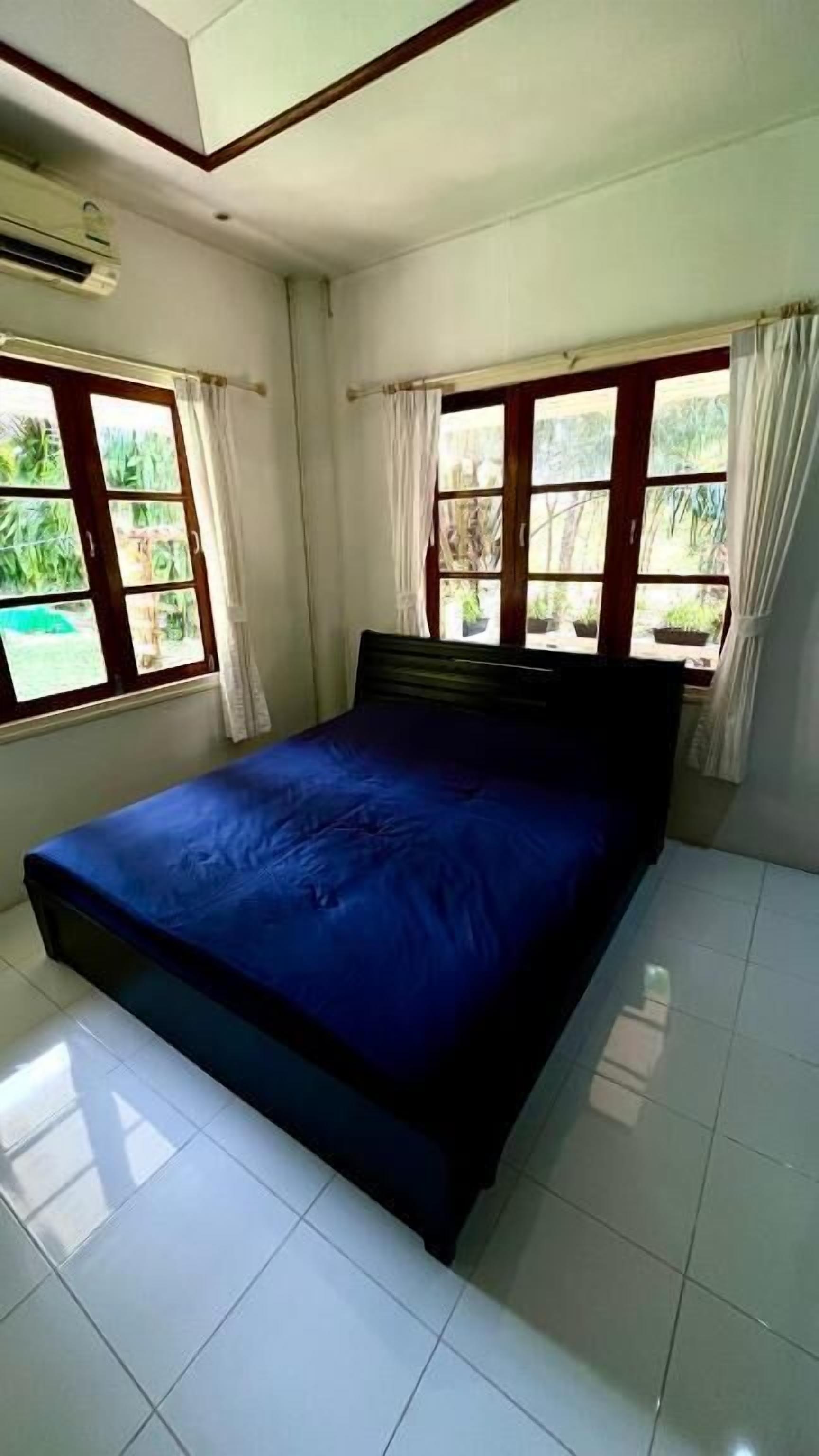 Un dormitorio con una cama, dos ventanas con cortinas y suelo de baldosas.