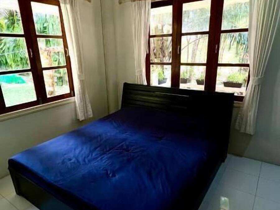 Un dormitorio con una cama, dos ventanas con cortinas y suelo de baldosas.