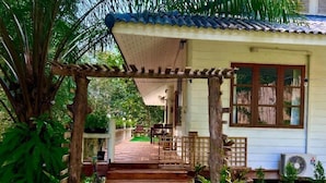 A wooden staircase leading to a house with a tiled roof, surrounded by lush greenery and a small patio area.
